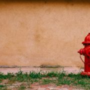 Red fire hydrant on the grass against a tan wall