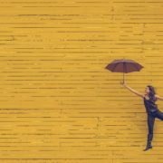Girl floating holding an umbrella in front of a yellow wall