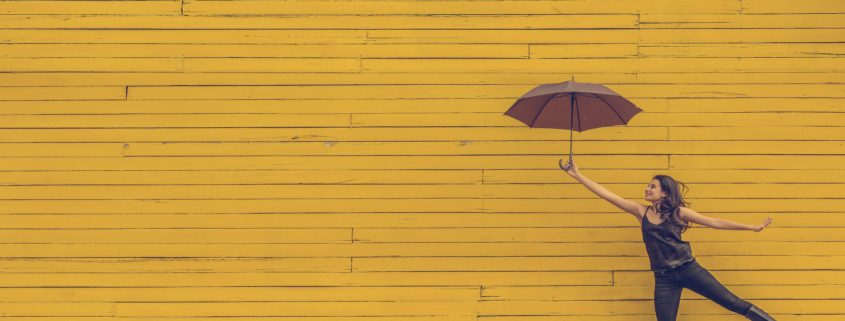 Girl floating holding an umbrella in front of a yellow wall