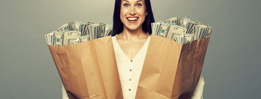 excited businesswoman holding two paper bags with money and smiling. photo in studio over grey background