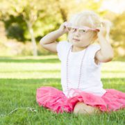 Little Girl Playing Dress In The Grass Up With Pink Glasses and Beaded Necklace.
