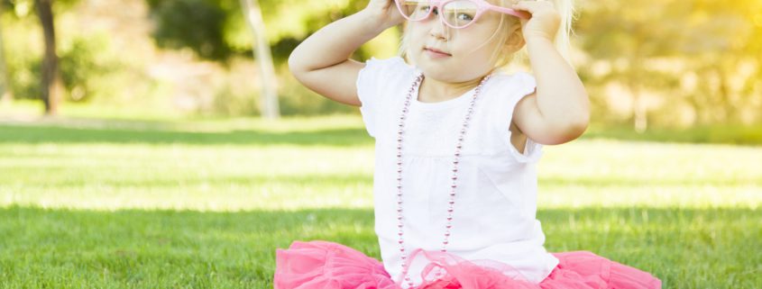 Little Girl Playing Dress In The Grass Up With Pink Glasses and Beaded Necklace.