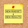 Yellow sticky note tacked on a cork board with 'New Mindset > New Results' written on it